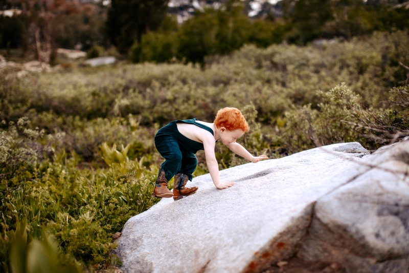 Family Photographer, a young red head boy climbs on a rock outside